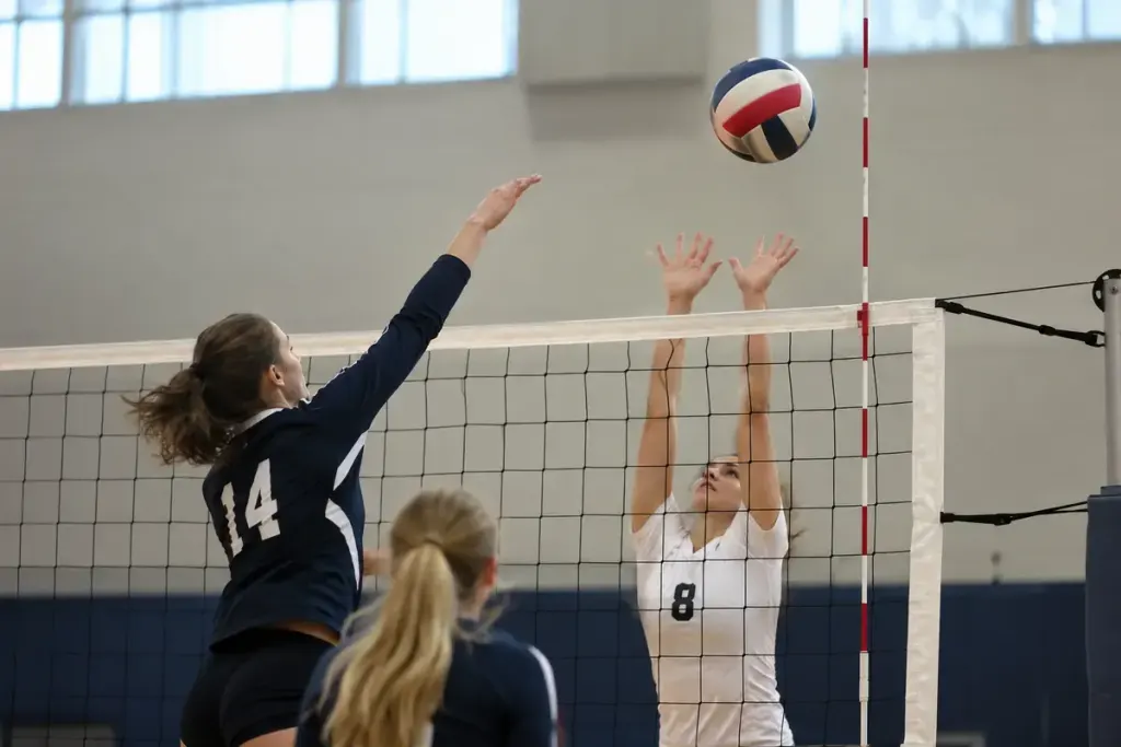 A volleyball net with a clearly visible red and white antenna and a ball near the court edge.
