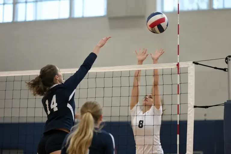A volleyball net with a clearly visible red and white antenna and a ball near the court edge.