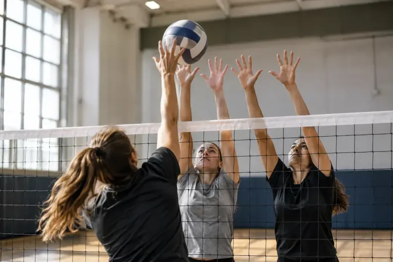 Volleyball players blocking ball at net in training gym.