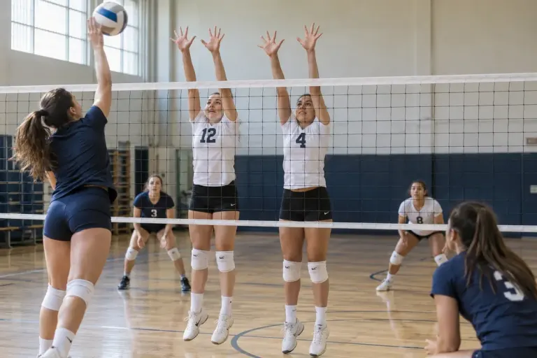 Volleyball training with two front-row blockers and back-court defenders positioned behind them, wide realistic gym view.