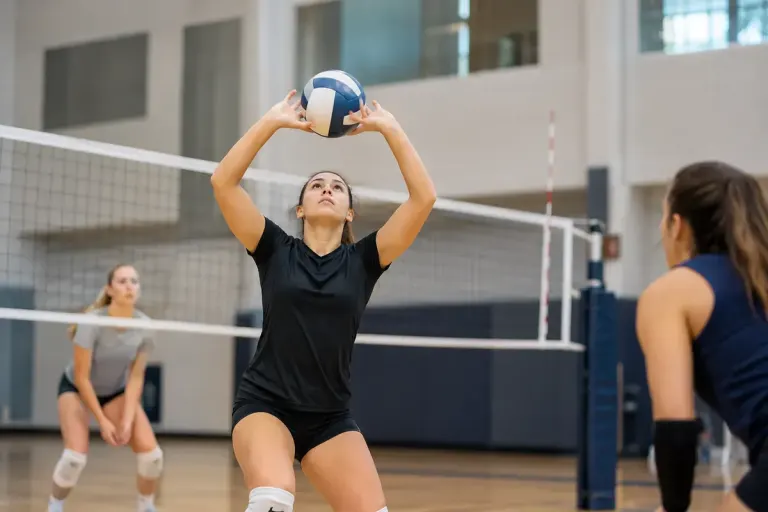 Volleyball player making overhead set on indoor practice court.